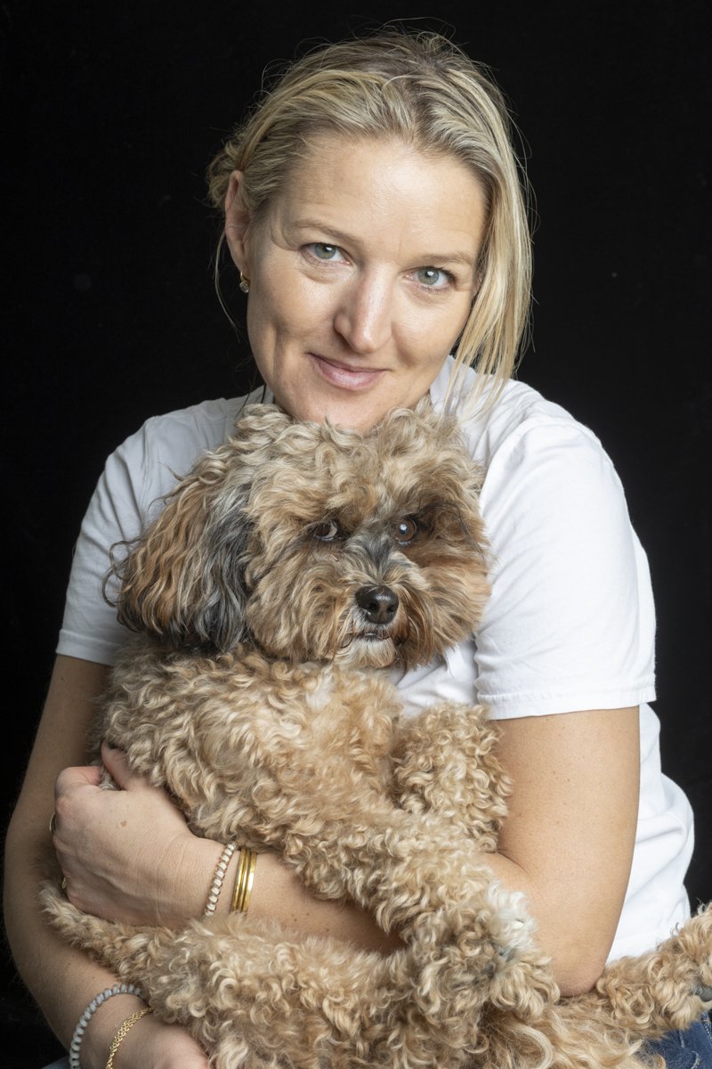 A smiling blonde woman holds her curly doodle in her arms.